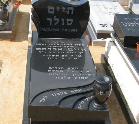 מצבה שחור עם כיתוב אפור בשילוב חריטת גלים לצד כד